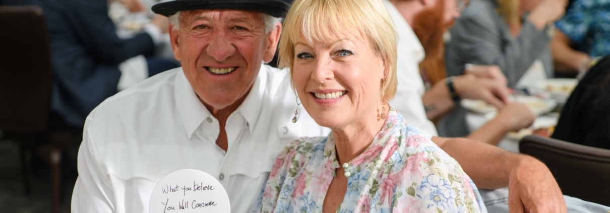 A man and a woman smile as they sit at a table.