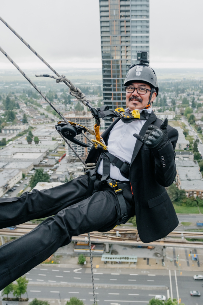 One Drop Zone rappeller hanging off the side of a building dressed in a black suit and white shirt