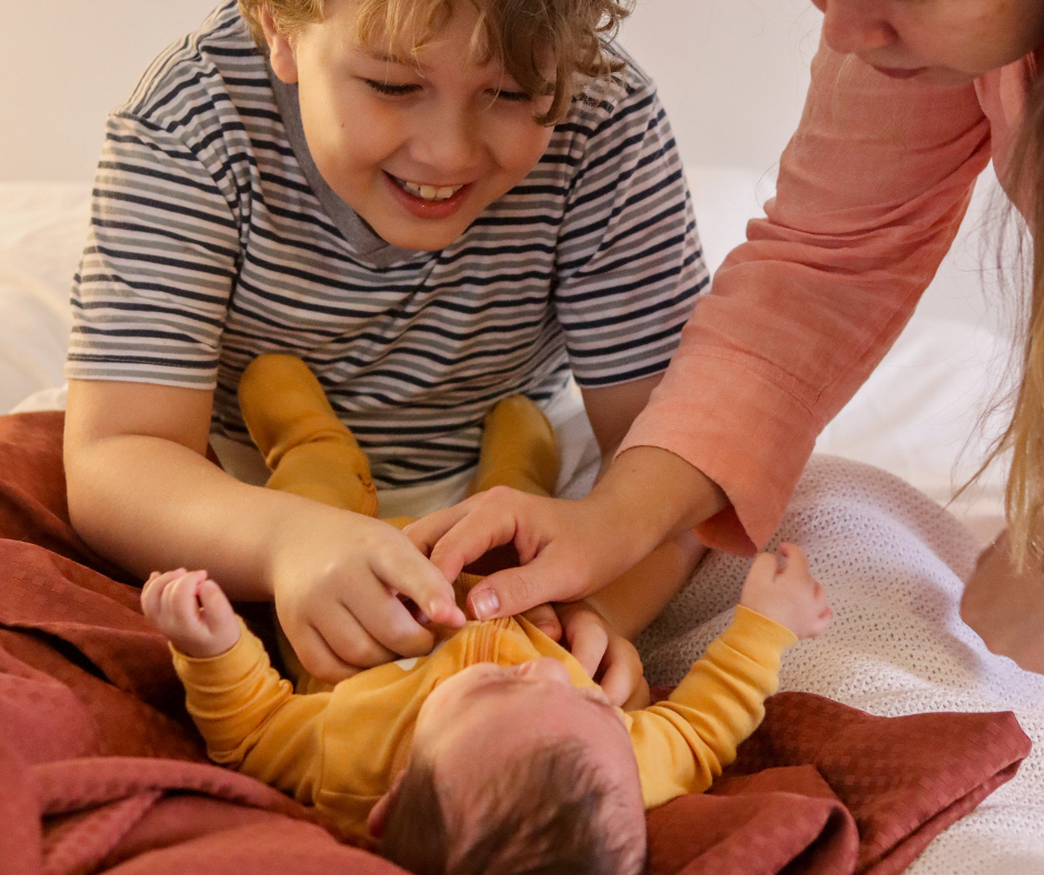 older brother tickling baby brother on bed